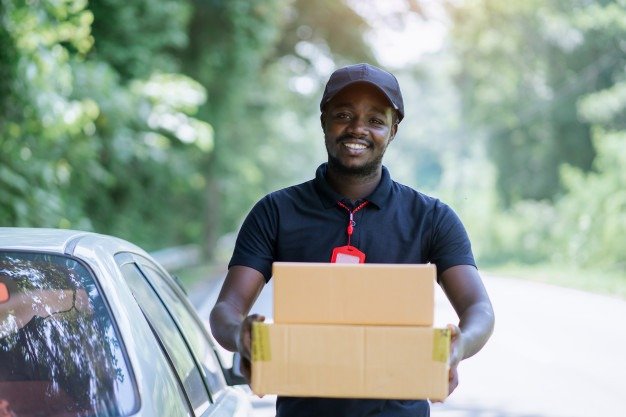 sourire-male-africain-courrier-livreur-messager-devant-voiture-livraison-colis_73622-995